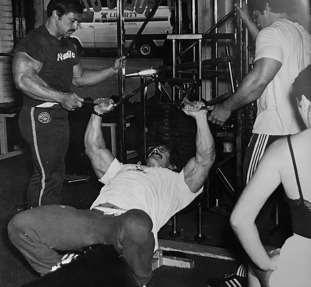 Casey Viator assists Mike Mentzer with forced reps on a Universal chest press machine